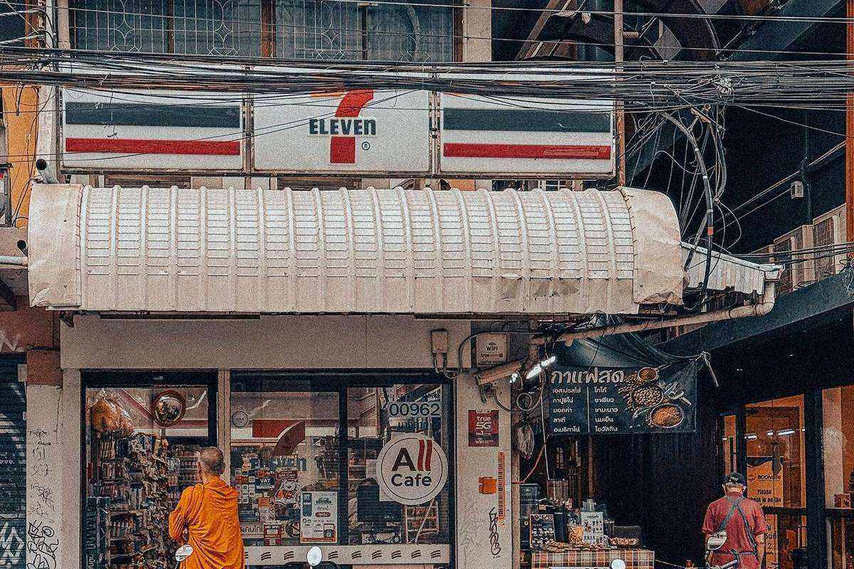A 7-Eleven shop front in Bangkok with a monk in orange robes standing outside